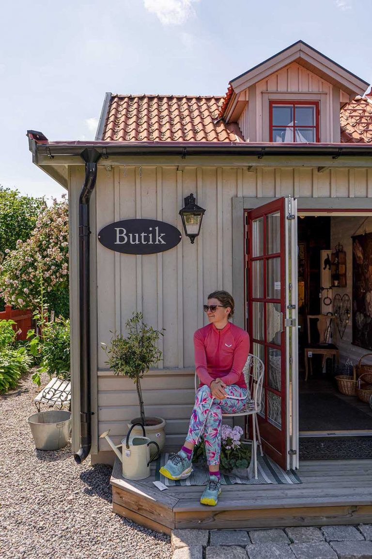 Die Bloggerin Judith Beck sitzt vor einer Butik in Schweden. Über ihr ist am beigen Haus ein Schild angebracht mit dem Wort Butik.