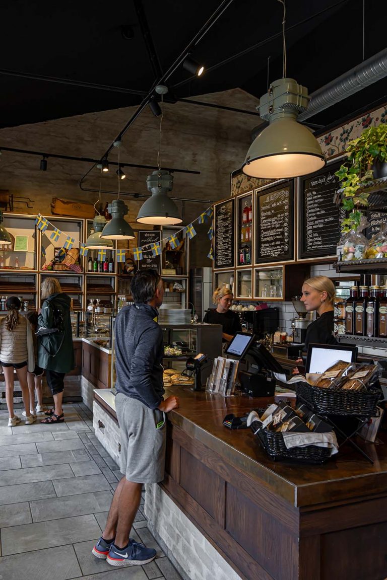 Der Blogger Jesús Tena ist in einem Schwedischen Café an der Theke und kauft frisches Brot. Der Raum ist in Brauntönen gehalten mit schönen Lampen dekoriert.