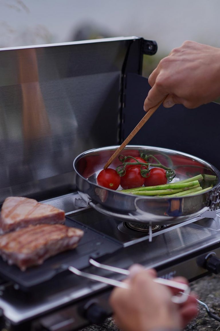 Ein Close-up von einem Campinggrill von Primus. Darauf wird gerade Fisch und Gemüse frisch zubereitet.